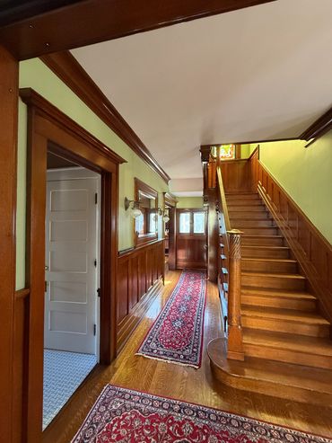 Wood-paneled hallway with red patterned rugs and a wooden staircase.