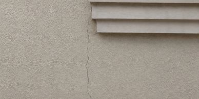 A narrow crack running vertically on a beige wall beneath horizontal slats.