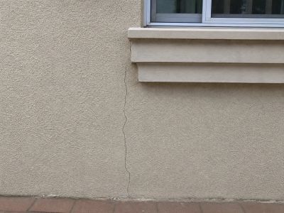 Vertical crack running down a beige exterior wall near a window.