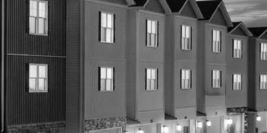 Row of townhouses warmly lit at dusk with garages and porch lights.