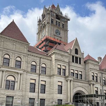 Historic stone building with a clock tower under renovation on a cloudy day.