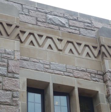 Stone building with intricate zigzag stonework near windows.