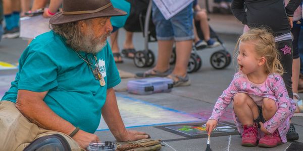 Little girl helping chalk artist and smiling