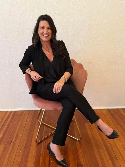 Woman in black suit sitting on a pink chair and smiling.