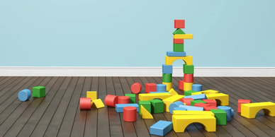 Colorful building blocks scattered on a wooden floor against a blue wall.