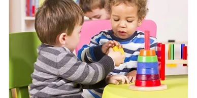Two toddlers playing with colorful stacking toys at a table.