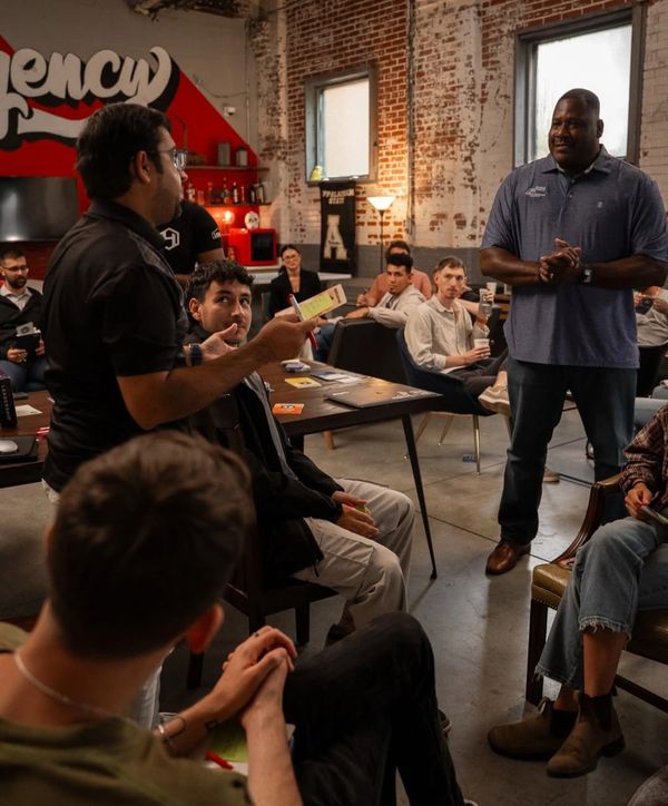 A group meeting in a casual, industrial-style room with brick walls and large windows.