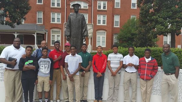 Group of young men and their mentors posing in front of a statue on a school campus.