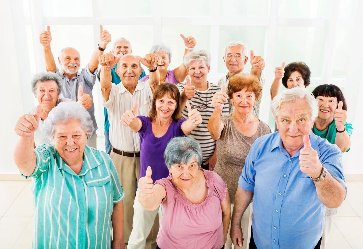 Group of happy elderly people showing thumbs up together indoors.