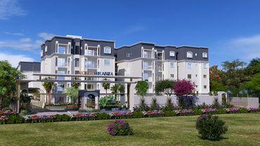 Modern apartment complex with landscaped gardens under a clear blue sky.