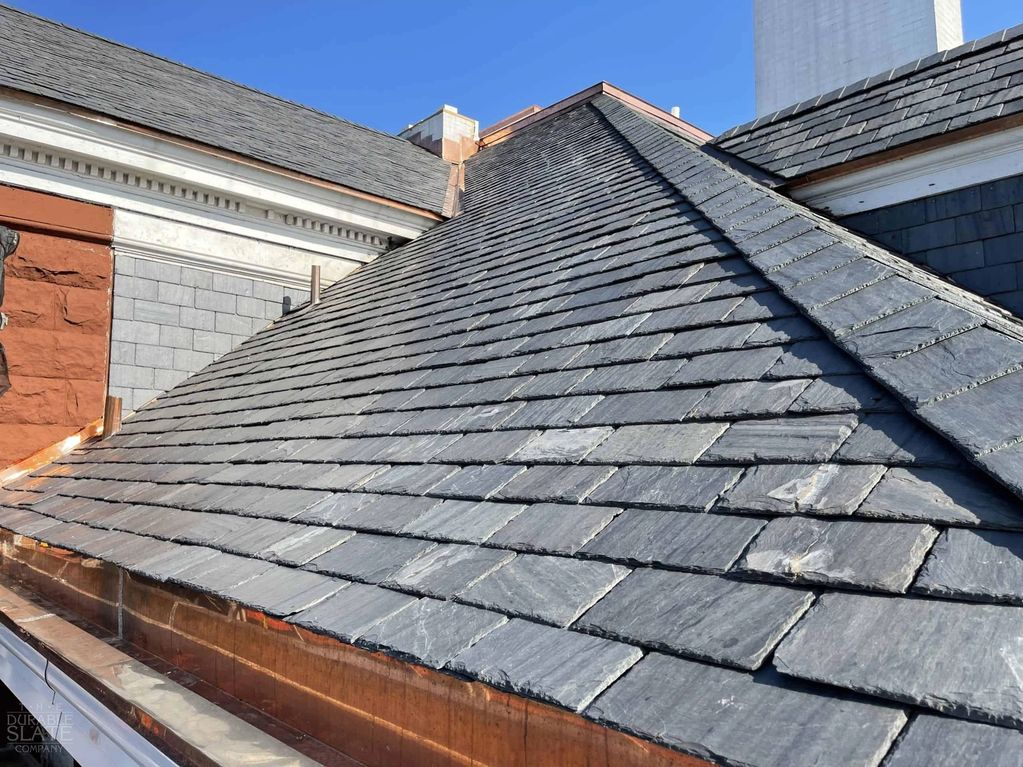 Slate roof with copper gutter under clear blue sky.