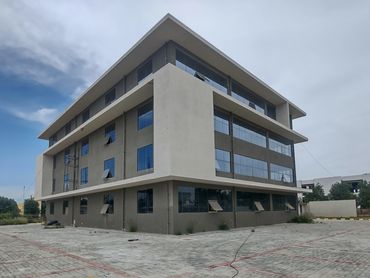 Modern four-story office building with large windows and paved surroundings.