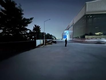 Nighttime scene outside a large industrial building with three people and a parked motorcycle.