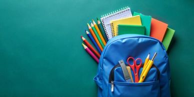 Blue backpack filled with school supplies against a green background.