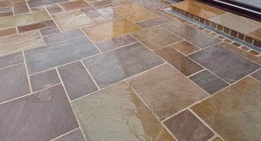 Wet stone patio with multicolored tiles leading to a doorstep.