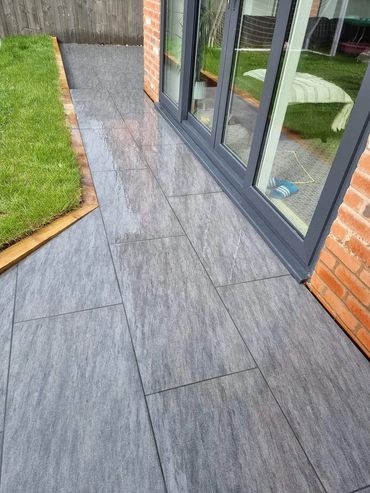 Wet gray tiles beside a glass door and green grass patch.