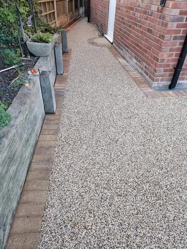 Clean and well-maintained pebble driveway next to a brick house and garden.