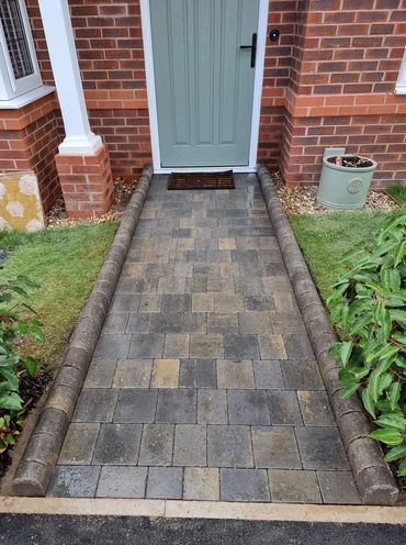 Neatly paved walkway leading to a light green front door with brick walls.
