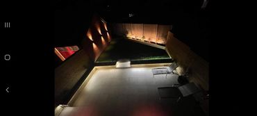 A cozy backyard patio lit with warm lights and two lounge chairs at night.