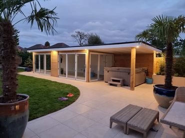 Modern backyard with a wooden cabin, hot tub, and palm trees at dusk.
