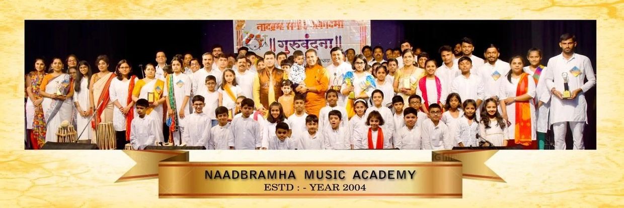 Group photo of Naadbramha Music Academy members, including children and adults, holding trophies.