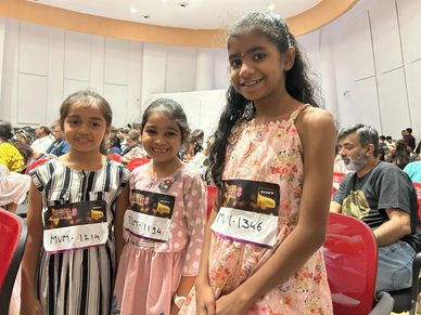 Three young girls smiling with audition tags at a singing competition.