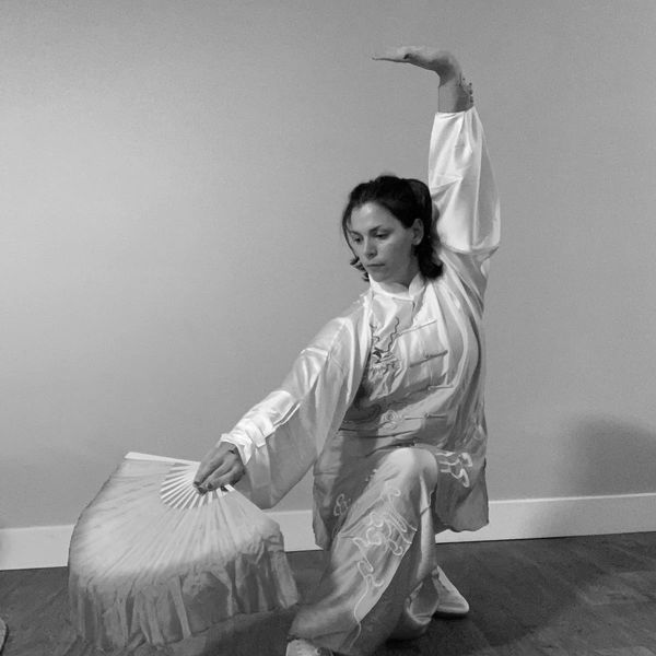 Woman performing traditional fan dance in orange and white attire.