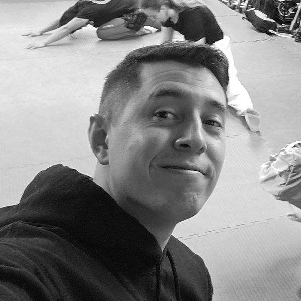 Man smiling in a gym with people stretching in the background.