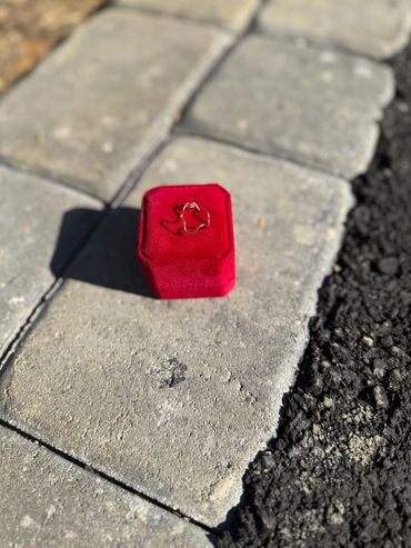 Gold ring on a red velvet box placed on stone pavement.