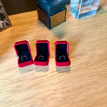 Three red velvet ring boxes with gold rings on a wooden table.