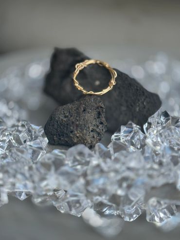 Gold ring on black volcanic rocks surrounded by clear crystals.