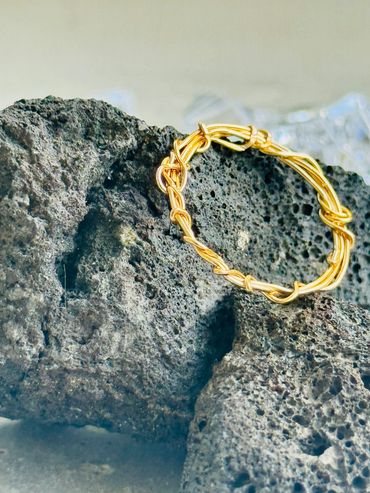 Intricately twisted gold wire bracelet resting on textured volcanic rock.