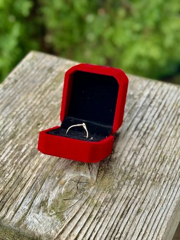 A delicate ring in a red velvet box on a wooden surface outdoors.