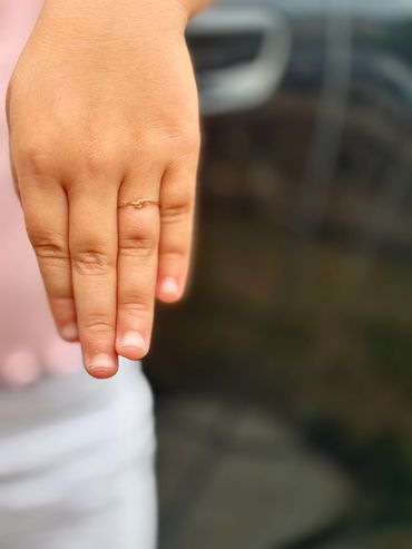 Hand wearing a delicate gold knot ring on the middle finger.