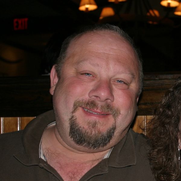 Smiling man with a goatee in a dimly lit setting.