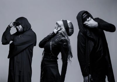 Three people in black clothing and blindfolds striking dramatic poses against a gray backdrop.