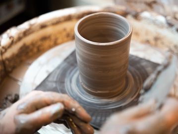 Potter making a handmade ceramic mug on the pottery wheel out of clay and glaze. 
