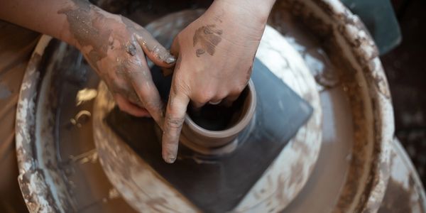 Handmade ceramic coffee mug being thrown from clay on pottery wheel by potter.