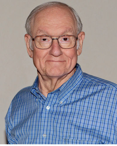 Elderly man with glasses smiling gently.