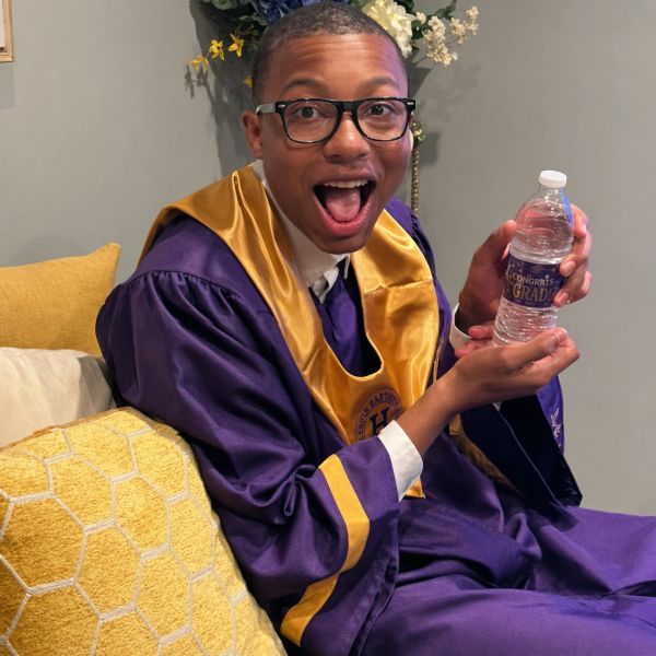 Excited graduate in purple and gold gown holding a congratulatory water bottle.