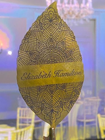 A decorative leaf with 'Elizabeth Hamilton' written, set in an elegant dining room.