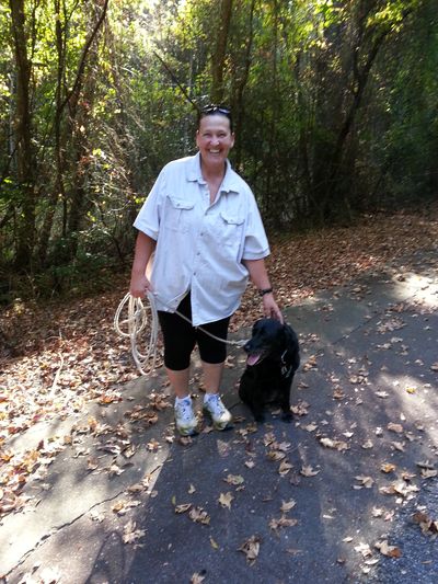 Dale Ward standing with black dog on leash, outdoors on a trail.