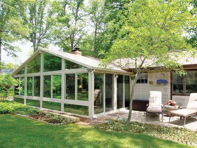 Large Gable Roof All Season Sunroom in Sandstone (light tan/brown) surrounded by bright green trees.