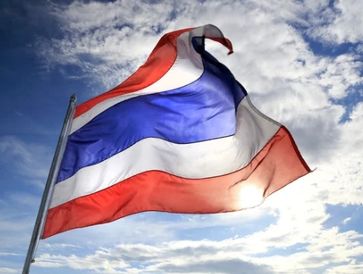 Thai flag waving in the wind against a clear blue sky.
