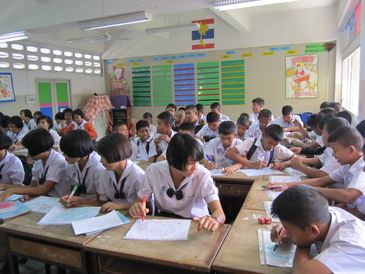 Thai students engaged in schoolwork inside a classroom.