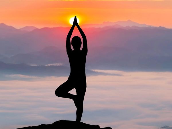 Silhouette practicing yoga at sunrise on a mountain.