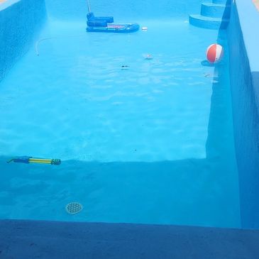 Empty blue swimming pool with a beach ball and float inside.