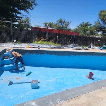 Man cleaning an empty swimming pool on a sunny day.