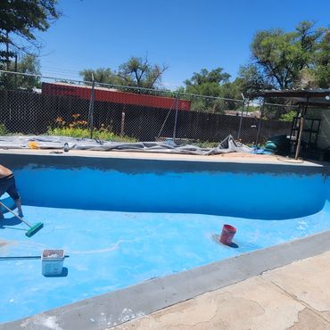 Man cleaning an empty swimming pool on a sunny day.