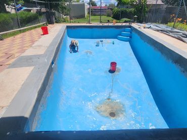 Person renovating an empty blue swimming pool under the sun.
